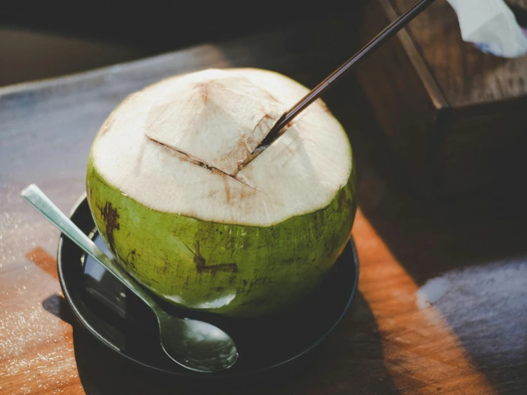 a green coconut sitting on top of a wooden table, by Emma Andijewska, trending on unsplash, with a straw, soup, sparkling in the sunlight, south east asian with long