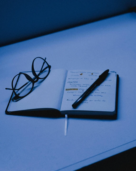 a notebook sitting on top of a table next to a pair of glasses, unsplash, ((blue)), lgbtq, dark. no text, multiple stories