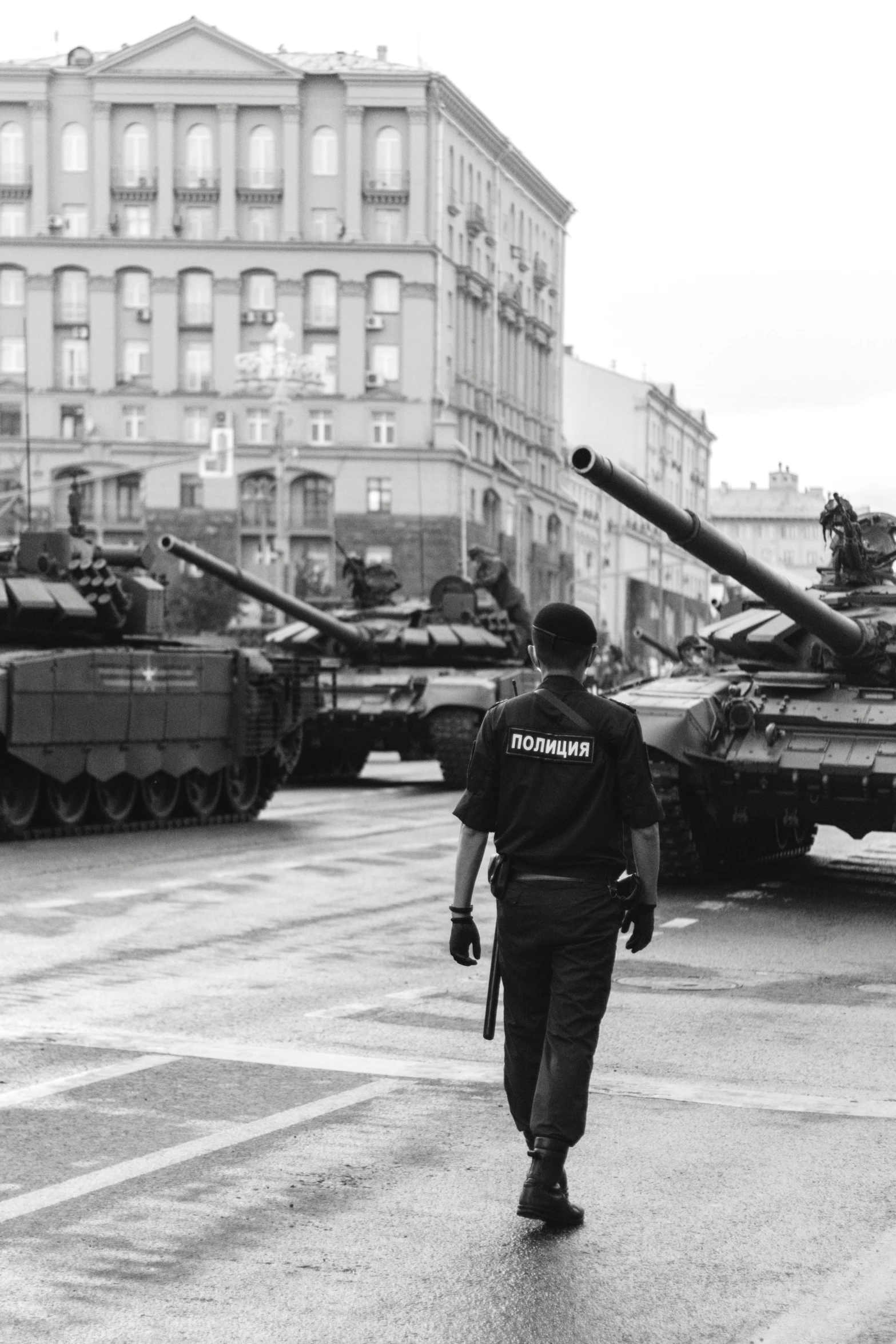 a black and white photo of a man walking in front of tanks, by Adam Marczyński, pexels contest winner, socialist realism, police officers under heavy fire, gta in moscow, taken in the late 2000s, military parade