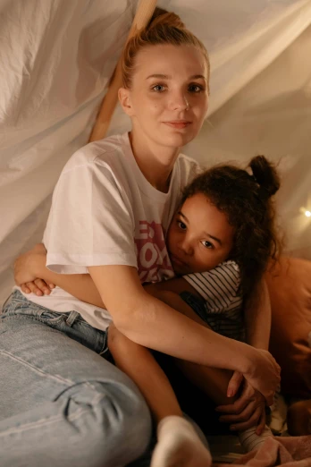 a woman sitting next to a little girl on a bed, jeans and t shirt, in a cave, holding each other, low quality photo