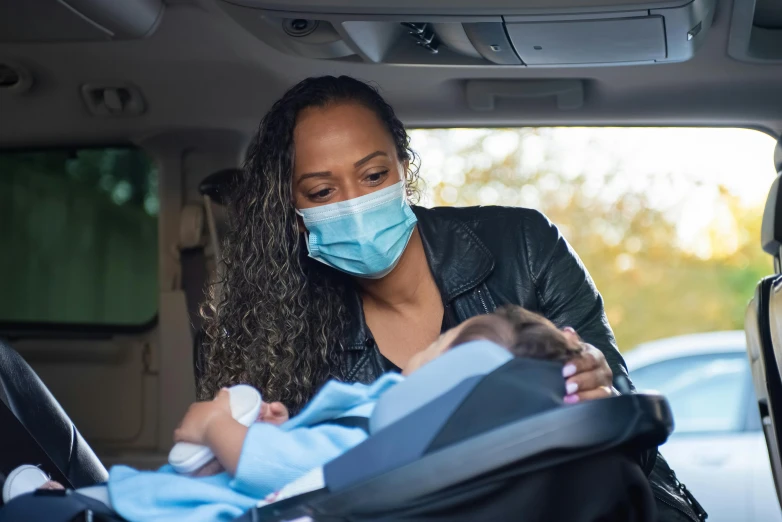 a woman in a face mask is holding a baby in a car seat, trending on pexels, happening, square, healthcare worker, essence, jonathan ivy