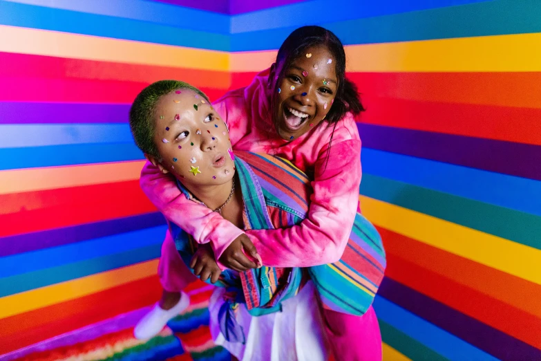 a woman holding a child in front of a colorful wall, an album cover, pexels contest winner, black arts movement, the room is raucous and joyful, lesbians, neon face paint, a bald