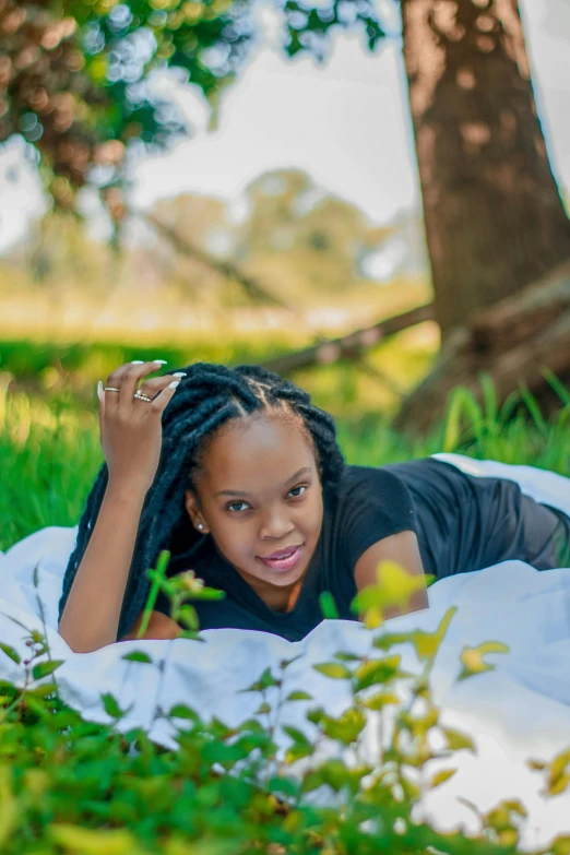 a woman laying on a blanket in the grass, by Arie Smit, pexels contest winner, black teenage girl, confident looking, next to a tree, casual pose