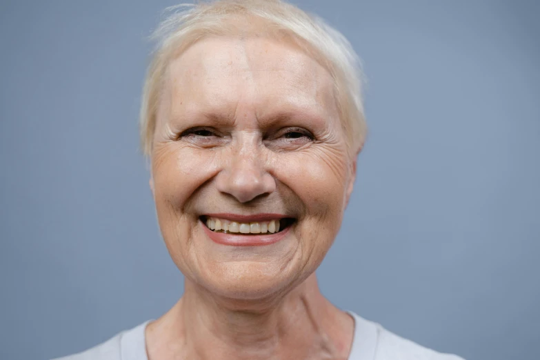 a woman with white hair smiling at the camera, on grey background, closed mouth showing no teeth, implants, smooth render