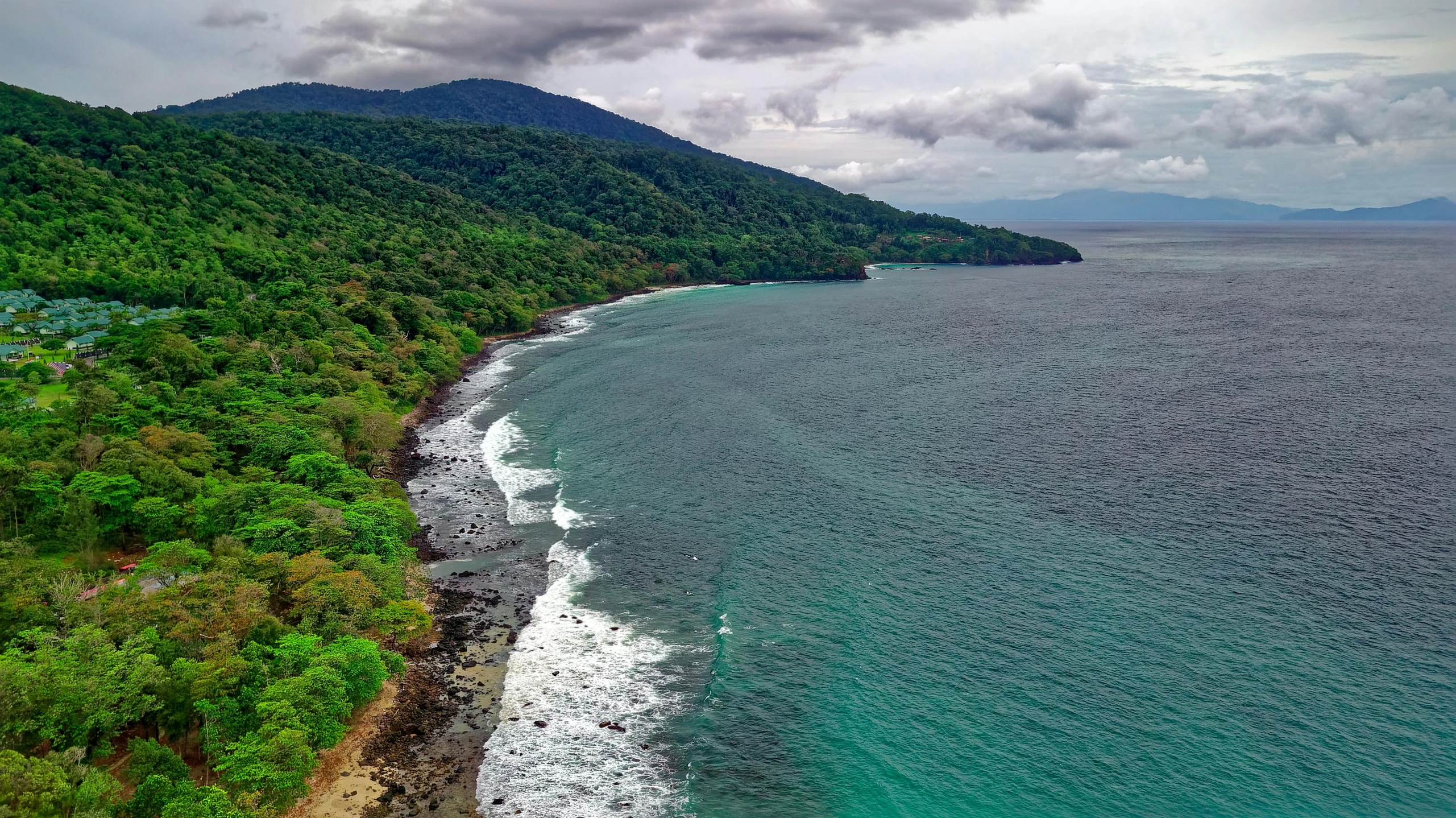 a large body of water next to a lush green hillside, inspired by Juan de Flandes, pexels contest winner, sumatraism, rocky seashore, drone photograpghy, tropical forest, grey