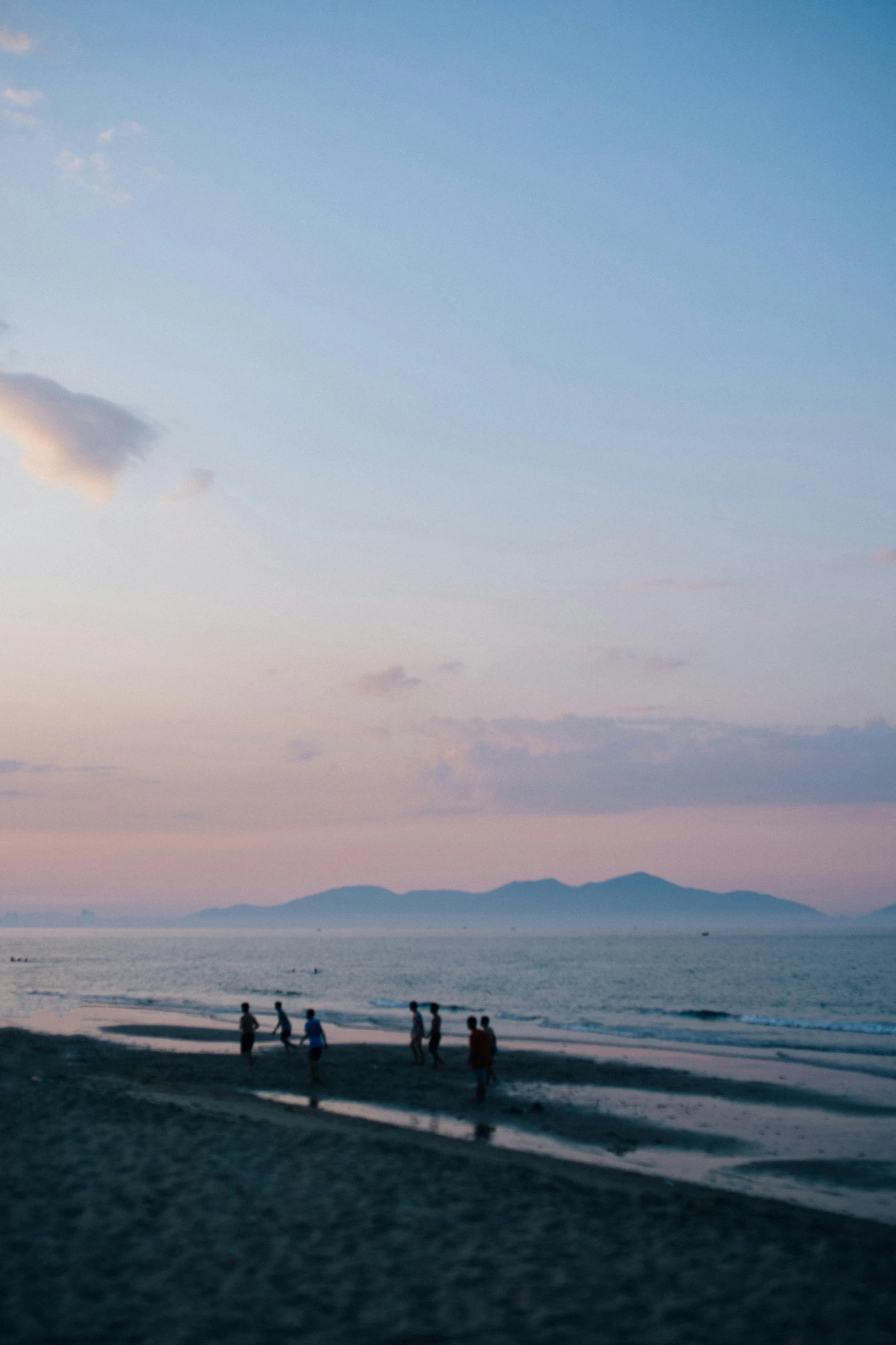 a group of people standing on top of a sandy beach, a picture, by Jang Seung-eop, unsplash, romanticism, late summer evening, guangjian, seen from afar, island in the background