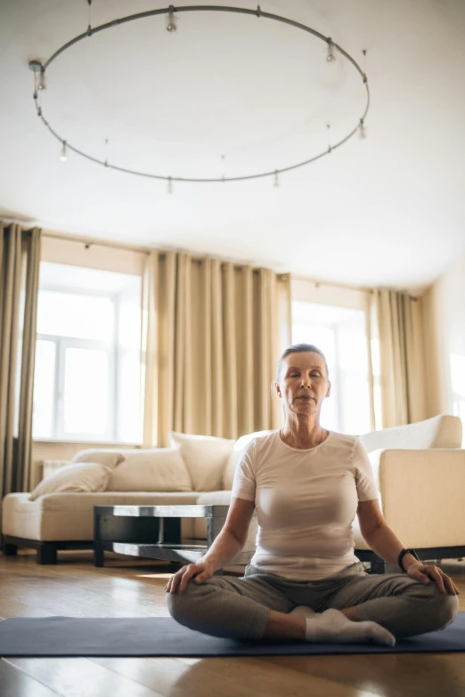 a man sitting on a yoga mat in a living room, a portrait, by Matthias Stom, unsplash, older woman, sitting on a lotus flower, in the center of the image, 4 k''