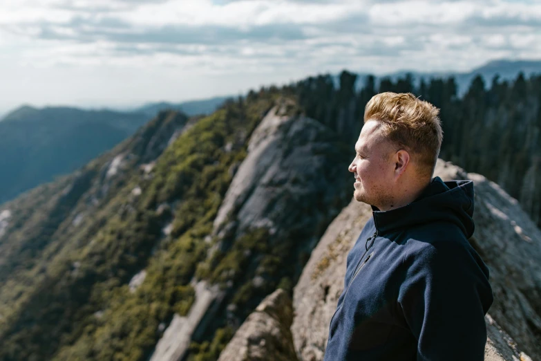 a man standing on top of a mountain next to a forest, a portrait, inspired by Seb McKinnon, pexels contest winner, looking to the side off camera, profile image, brittney lee, angle profile portrait