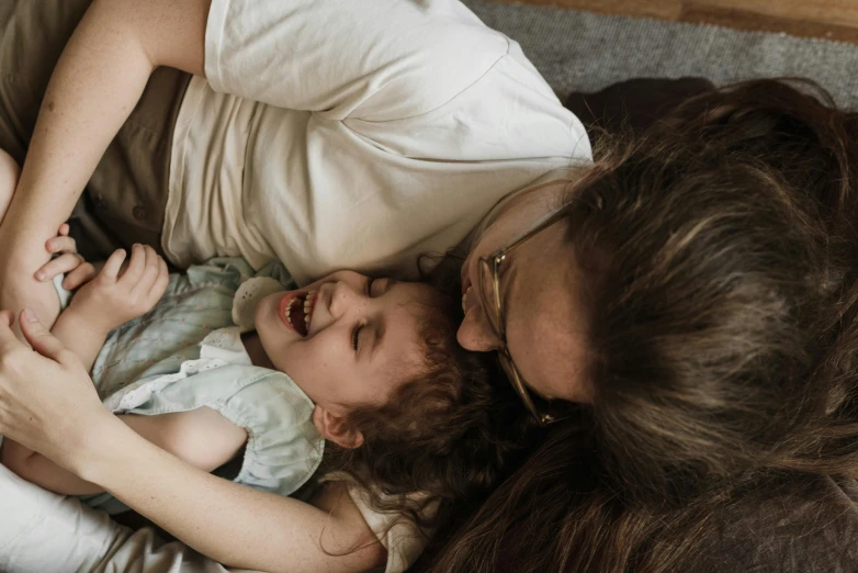 a woman laying on top of a bed holding a baby, pexels contest winner, incoherents, head bent back in laughter, avatar image, high angle close up shot, thumbnail