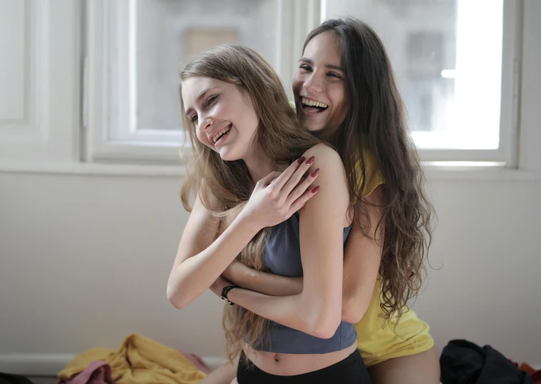 a couple of women standing next to each other, a picture, trending on pexels, the room is raucous and joyful, young with long hair, bralette, hugging her knees