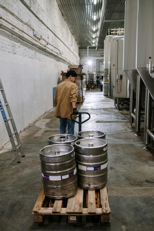 a man standing next to two kegs on a pallet, unsplash, process art, back room, facing away, stainless steal, walking to the right