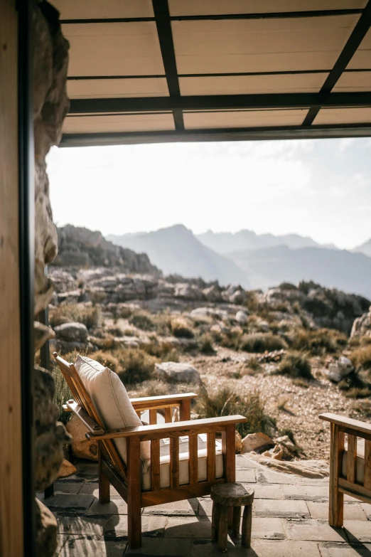 a couple of wooden chairs sitting on top of a stone floor, by Simon Marmion, trending on unsplash, interior of a mountain hut, balcony door, desert setting, sitting in a lounge