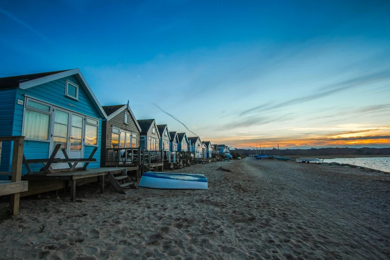 a row of beach huts sitting on top of a sandy beach, by Julian Allen, unsplash contest winner, golden hour 8k, cottage town, blue, vibrant lights