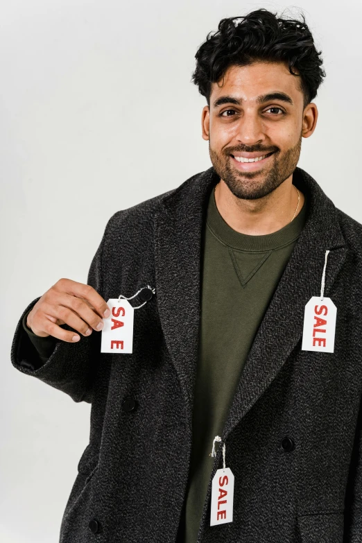 a man holding two tags with the word sale written on them, pexels contest winner, happening, wearing a duster coat, mkbhd, promotional photoshoot, smiling