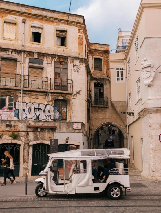 a tuk - tuk parked in front of a building with graffiti on it, a photo, by Matija Jama, pexels contest winner, the city of lisbon, overlooking, a blond, dua lipa