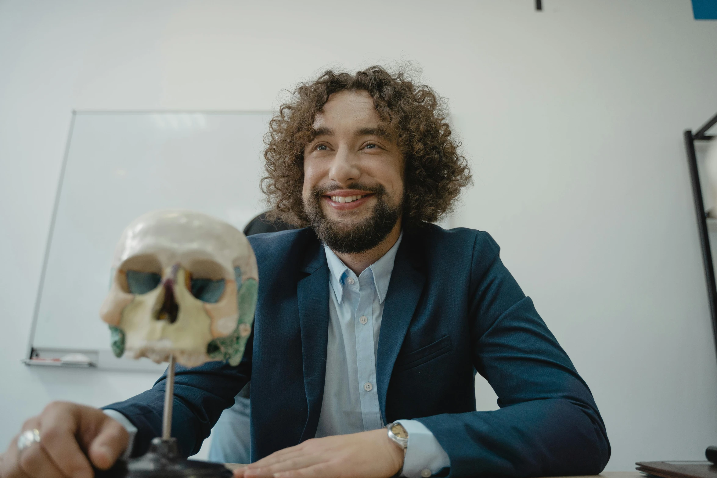 a man sitting at a table with a skull in front of him, featured on reddit, three hairy neanderthal people, professional profile photo, in a classroom, smiling male