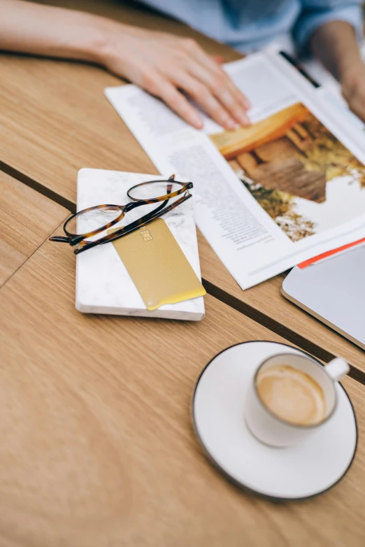 a person sitting at a table with a laptop and a cup of coffee, private press, marble and hint gold, wearing gold glasses, business card, guide