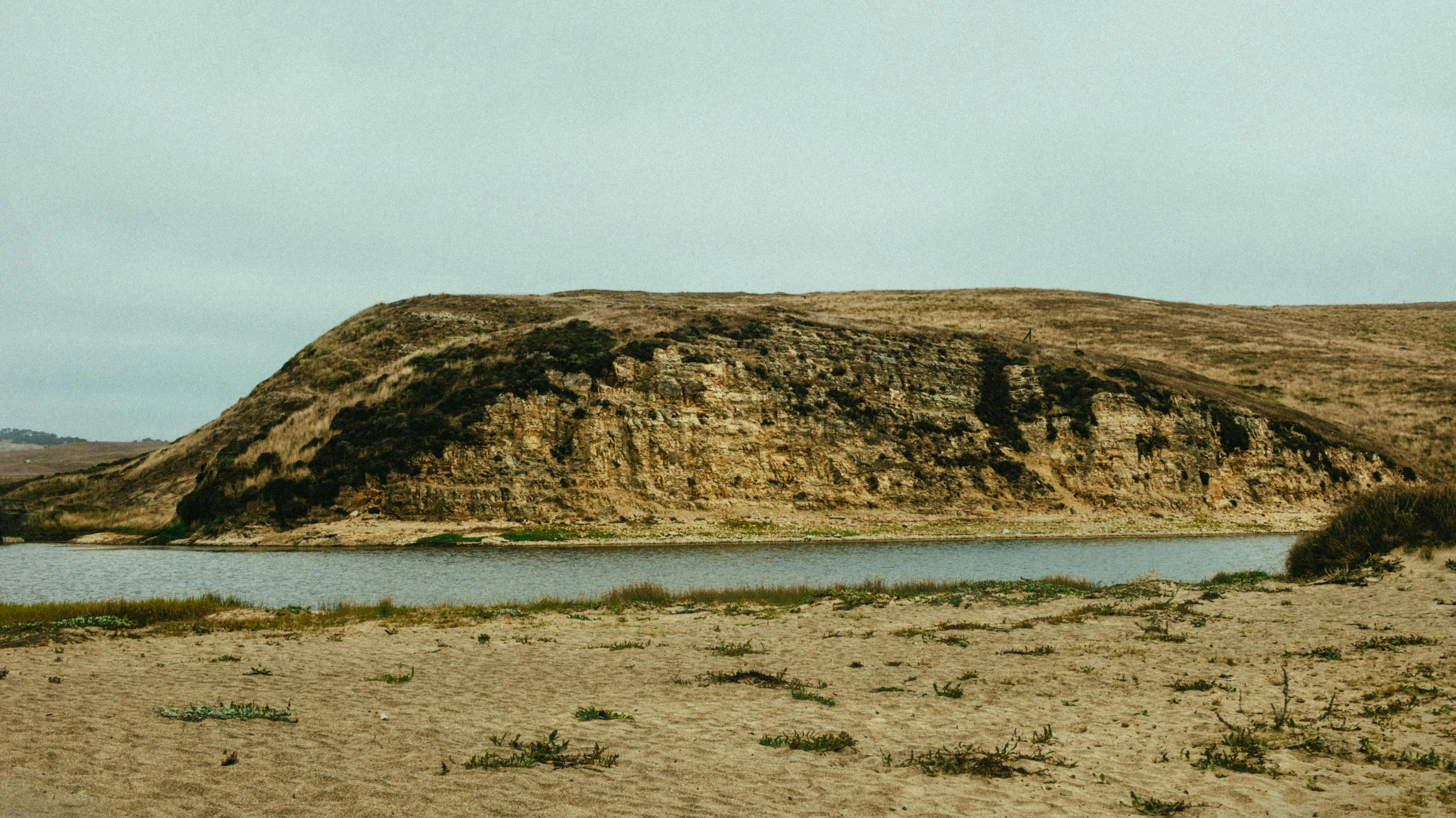 a body of water sitting on top of a sandy beach, by Elsa Bleda, unsplash, land art, hillside, prairie, background image, high cliff