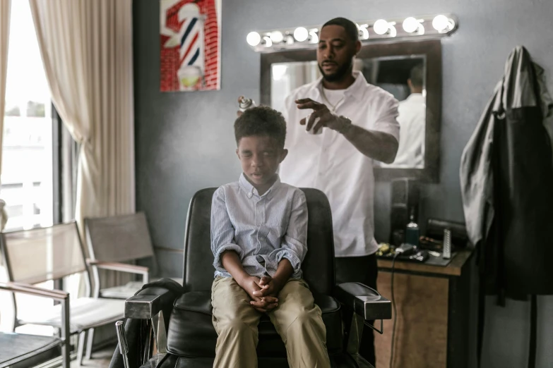 a man cutting a young boy's hair in a barber shop, pexels contest winner, essence, sitting in a chair, modeling, moviestill