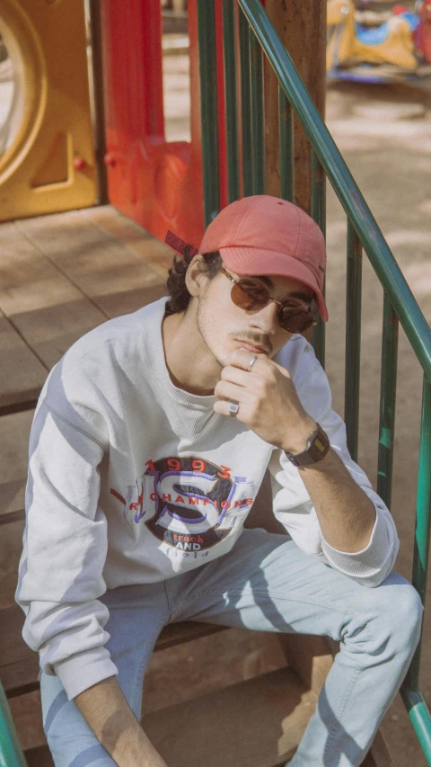 a man sitting on the steps of a playground, an album cover, by Andrew Stevovich, trending on pexels, aestheticism, wearing sunglasses and a cap, faded red colors, male ulzzang, profile image