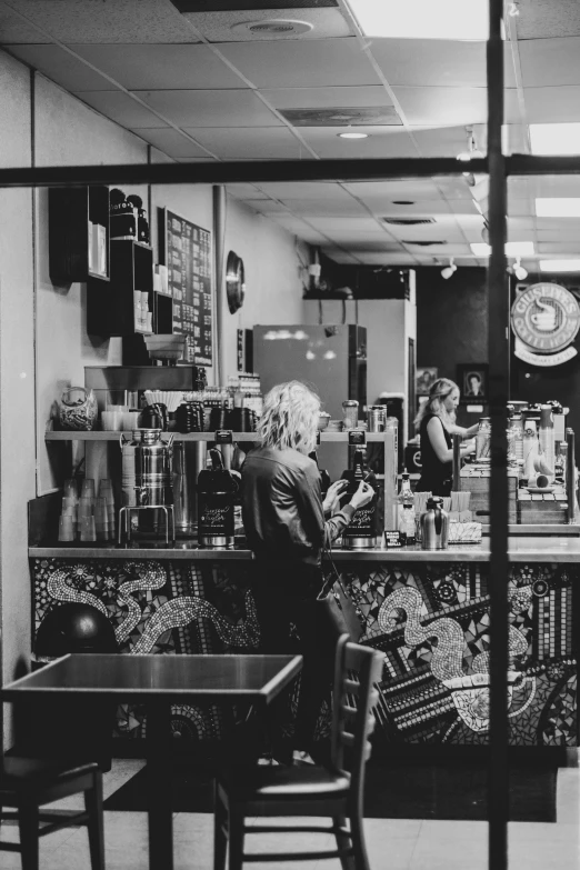 a black and white photo of a woman sitting at a table, by Tom Bonson, pexels contest winner, thanos as a starbucks barista, panoramic view of girl, robert plant, coffee machine