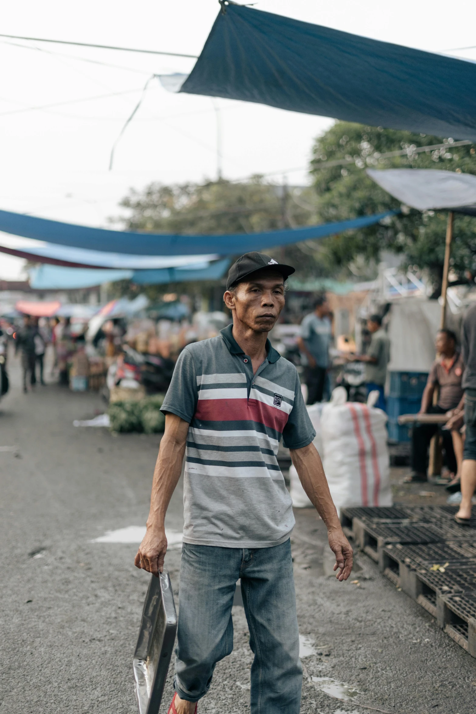 a man walking down a street holding a skateboard, by Jan Tengnagel, trending on unsplash, happening, fish market stalls, indonesia, square, looking threatening