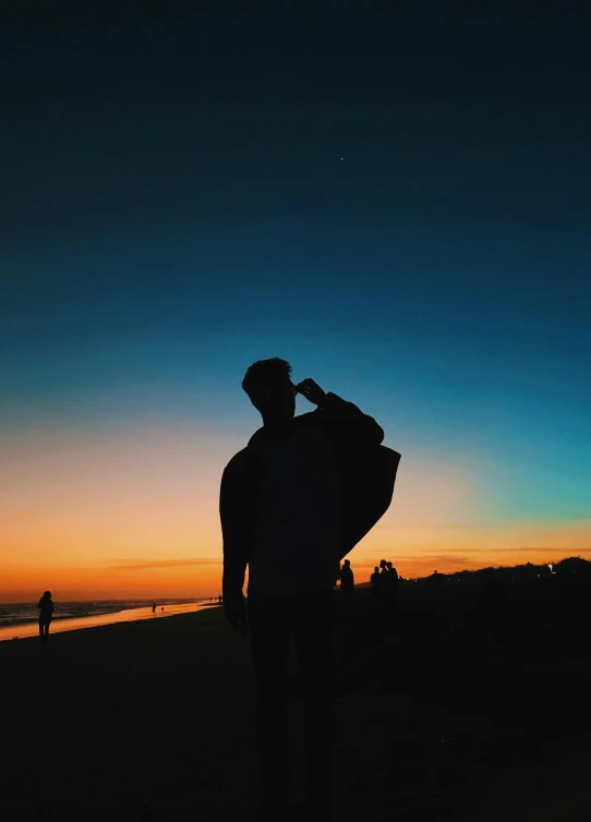 a man standing on top of a beach holding a surfboard, pexels contest winner, character silhouette, cloak covering face, calm night. over shoulder shot, profile pic
