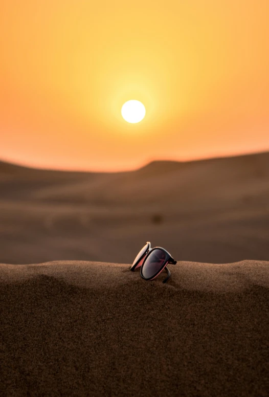 a pair of sunglasses sitting on top of a sand dune, the sunset, dubai, shot with sony alpha, high-quality photo