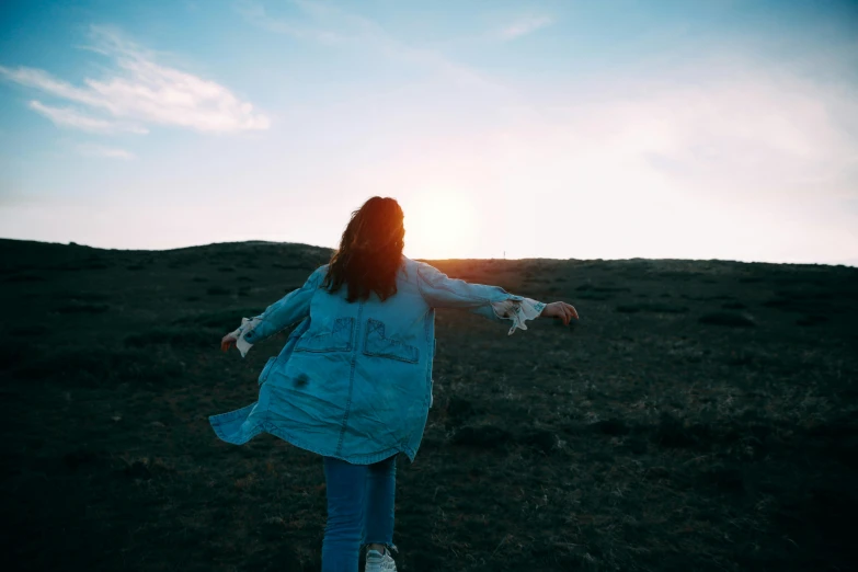 a woman standing on top of a grass covered field, pexels contest winner, happening, wearing a jeans jackets, back lit, teal aesthetic, girl is running