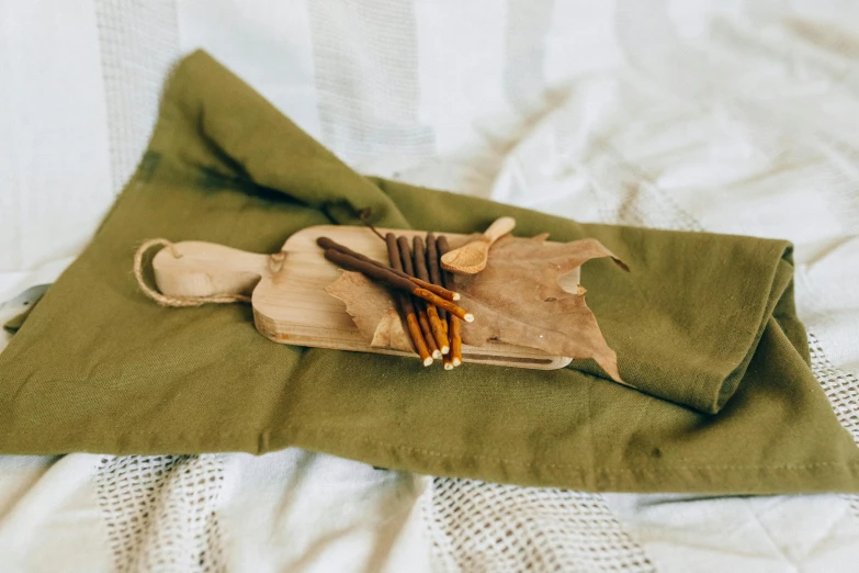 a wooden cutting board sitting on top of a green cloth, by Emma Andijewska, hurufiyya, holding a wooden staff, ocher details, folded, miniature product photo