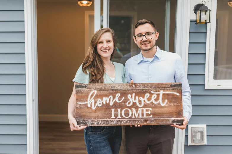 a man and woman holding a sign that says home sweet home, a portrait, avatar image, tyler west, professional photograph, background image