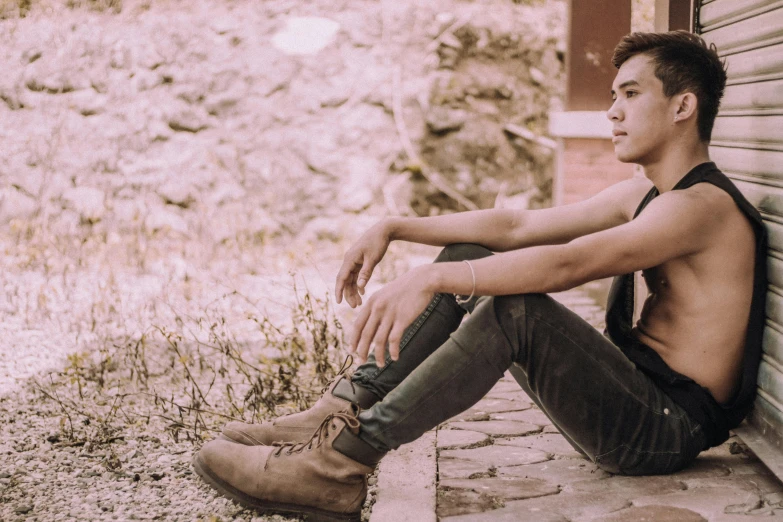 a shirtless young man sitting on the side of a building, an album cover, trending on pexels, realism, brown boots, background image, attractive androgynous humanoid, profile pic