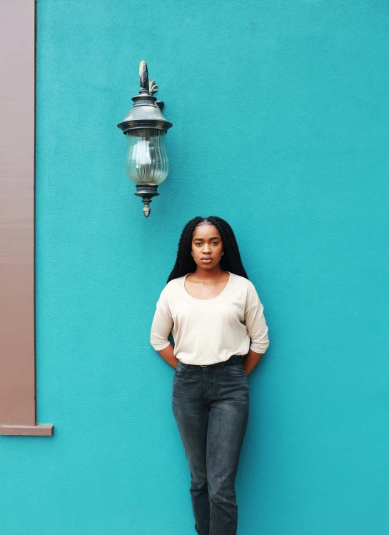 a woman standing in front of a blue wall, by Chinwe Chukwuogo-Roy, wearing a dark shirt and jeans, alexis franklin, ambient teal light, instagram post