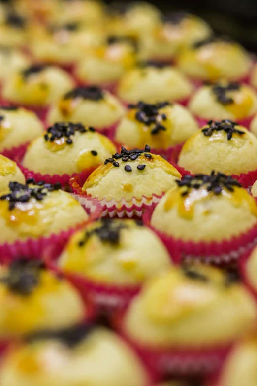 a tray of yellow cupcakes with black sprinkles, hurufiyya, medium shot angle, bao pnan, brazilian, cannonballs