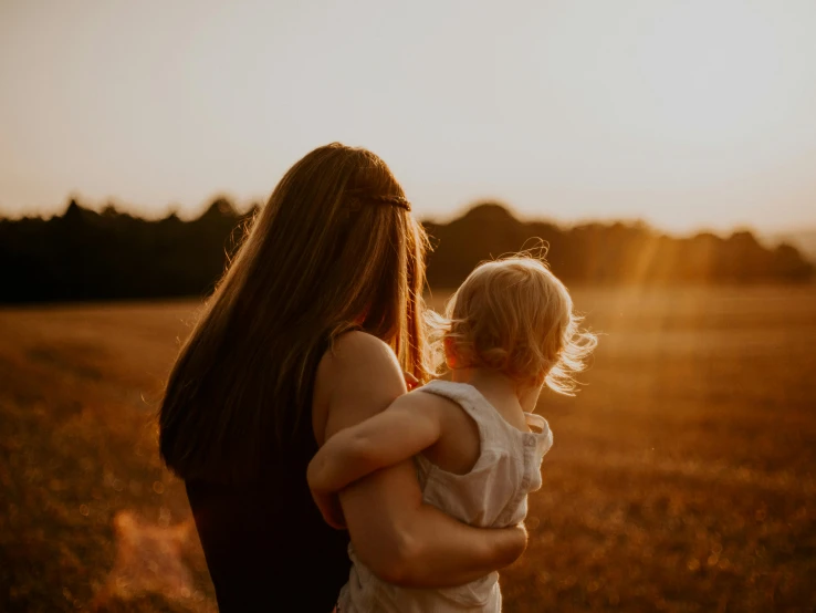 a woman holding a small child in a field, pexels contest winner, evening sun, over the shoulder, high quality upload, looking outside