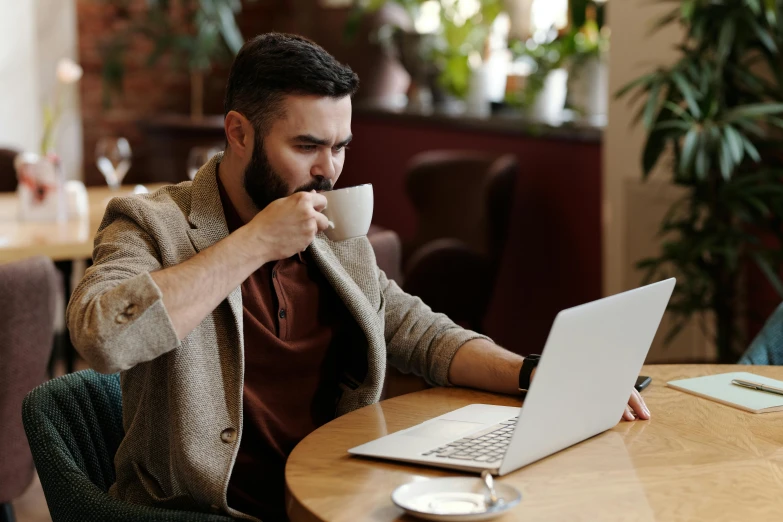 a man sitting at a table with a laptop and a cup of coffee, a screenshot, pexels, figuration libre, aboriginal australian hipster, eating, doing an elegant pose, brown