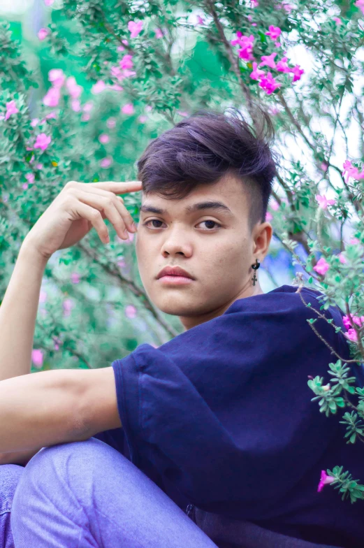 a young man sitting in front of a bush of flowers, inspired by Jorge Jacinto, unsplash, androgynous face, dzung phung dinh, looking to camera, lgbt