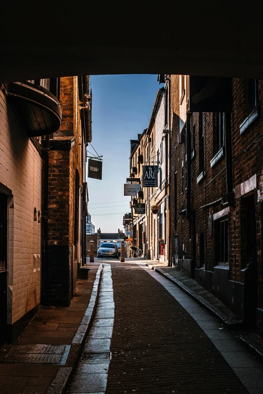 a narrow street lined with tall brick buildings, by IAN SPRIGGS, pexels contest winner, evening sunlight, warehouses, archway, blue