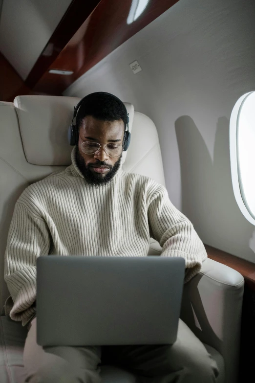 a man sitting in an airplane with a laptop, afrofuturism, jaylen brown, overcast, floating headsets, corporate boss