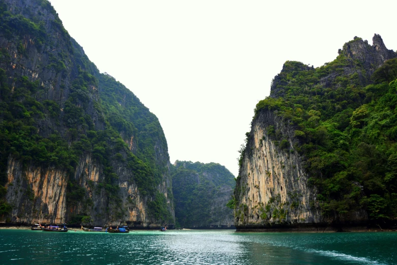 a couple of boats that are in the water, pexels contest winner, hurufiyya, sheer cliffs surround the scene, south east asian with long, multicoloured, 2000s photo