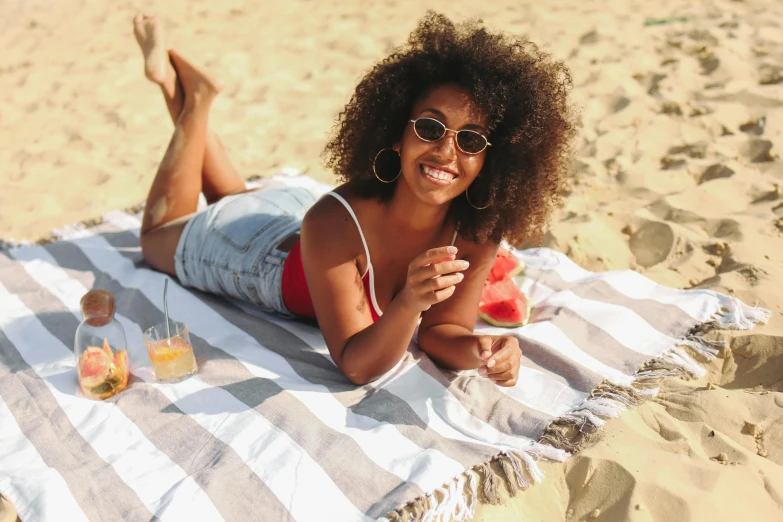 a woman laying on a beach with a slice of watermelon, pexels contest winner, with afro, wearing a towel, vanessa morgan, al fresco