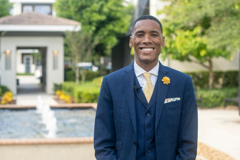 a man in a suit and tie standing in front of a fountain, cg society contest winner, alexis franklin, welcoming smile, blue gold suit, in his suit