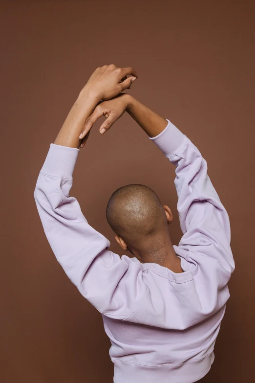 a man that is standing up with his hands in the air, inspired by Anna Füssli, trending on pexels, brown buzzcut, wearing a purple sweatsuit, showing her shoulder from back, muted pastels