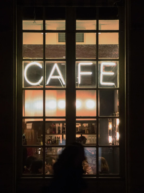 a person sitting at a table in front of a window, a photo, inspired by Elsa Bleda, trending on unsplash, nightcafe, bright signage, profile image, entrance