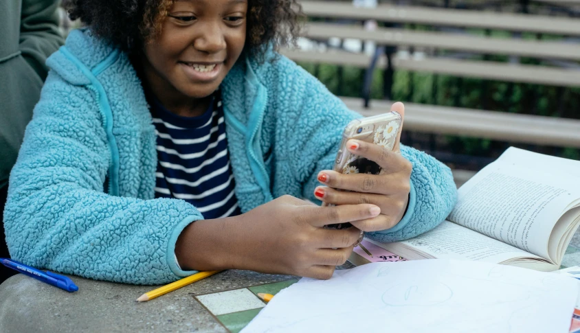 a woman sitting at a table using a cell phone, a picture, trending on pexels, happening, kids drawing, black teenage girl, a still of a happy, flattened