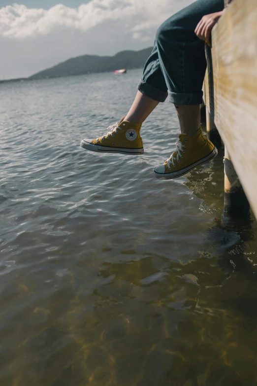 a person sitting on a dock next to a body of water, happening, sneakers, yellow carpeted, rough water, cinematic