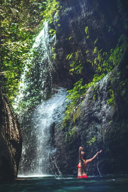 a woman in a bikini standing in front of a waterfall, with a tall tree, lush rainforest, yoga, sun lit