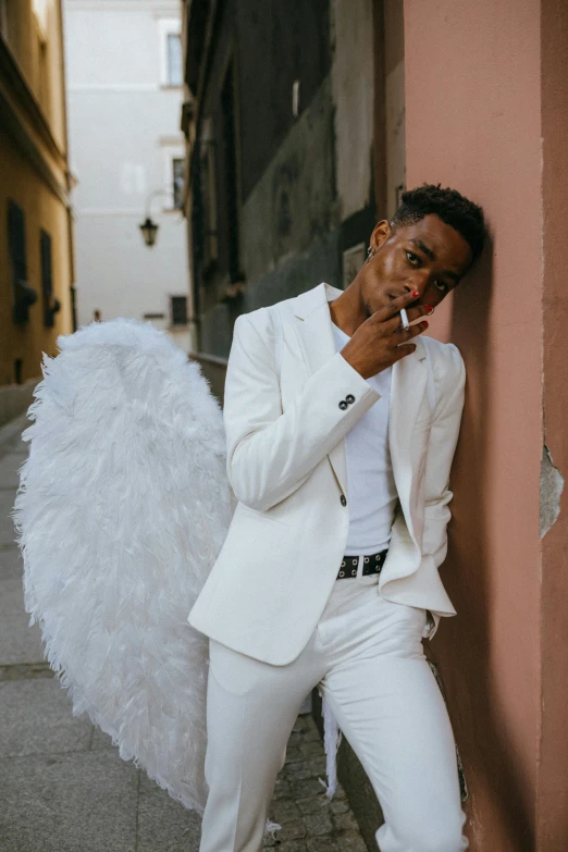 a man in a white suit leaning against a wall, an album cover, inspired by Ángel Botello, pexels contest winner, big angel wings wide open, black teenage boy, an epic non - binary model, in spain