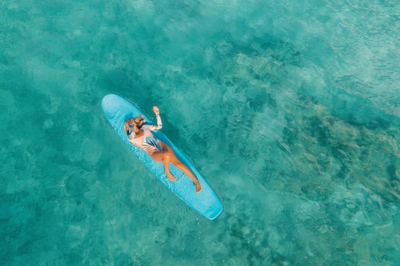 a woman riding on top of a surfboard in the ocean, flatlay, teal skin, great barrier reef, conde nast traveler photo