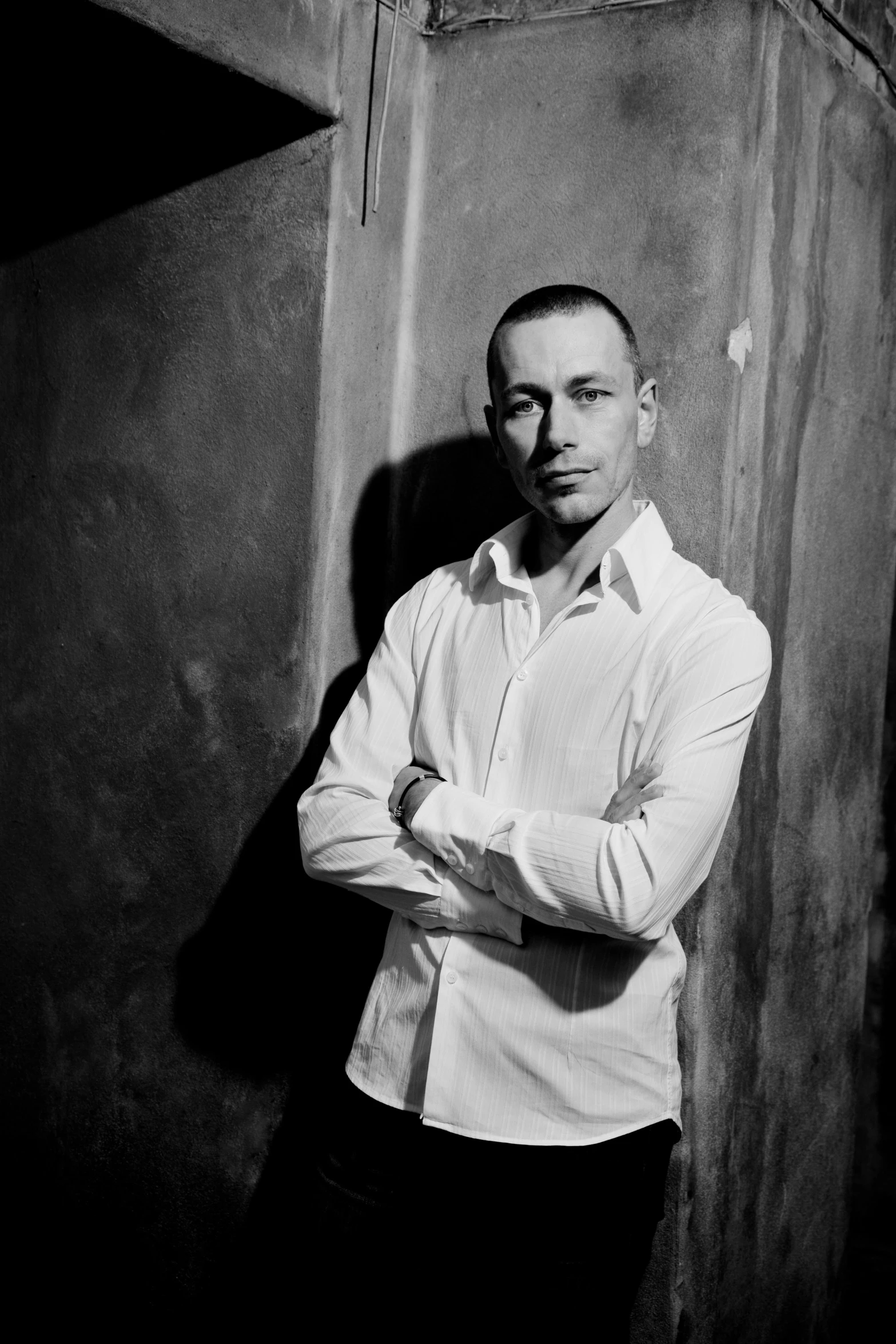 a black and white photo of a man leaning against a wall, inspired by Dmitry Levitzky, portrait of chester bennington, wearing a white button up shirt, artem, demur